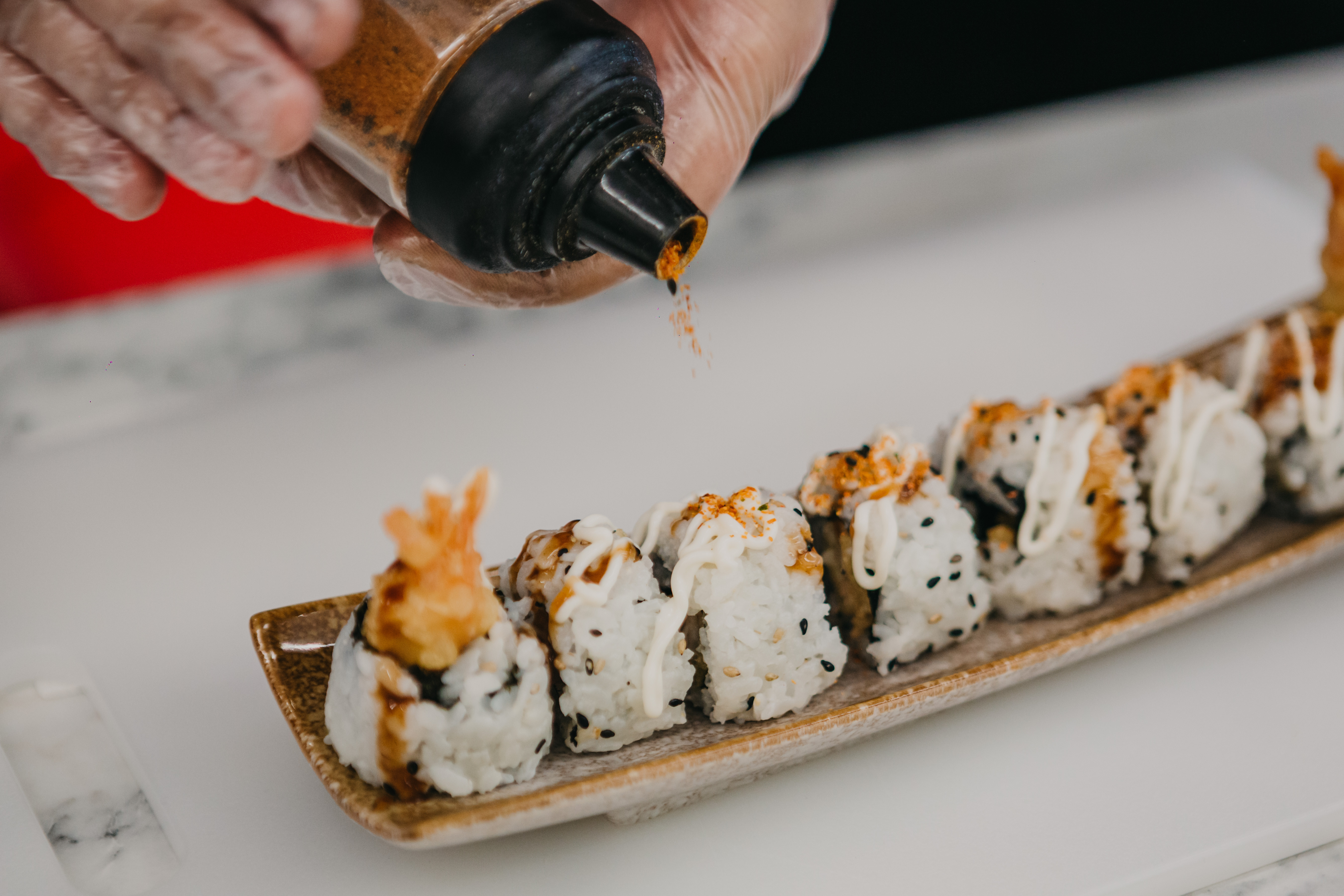 Close up of a person sprinkling seasoning onto a row of sushi rolls